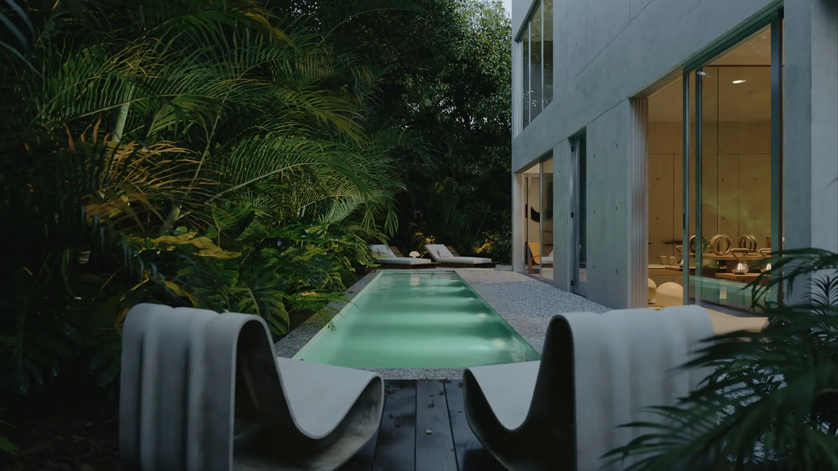 A render of the pool terrace at dusk: a long lap pool with a sculpted concrete edge, dense tropical planting, and the lit glass wall of the living room beyond